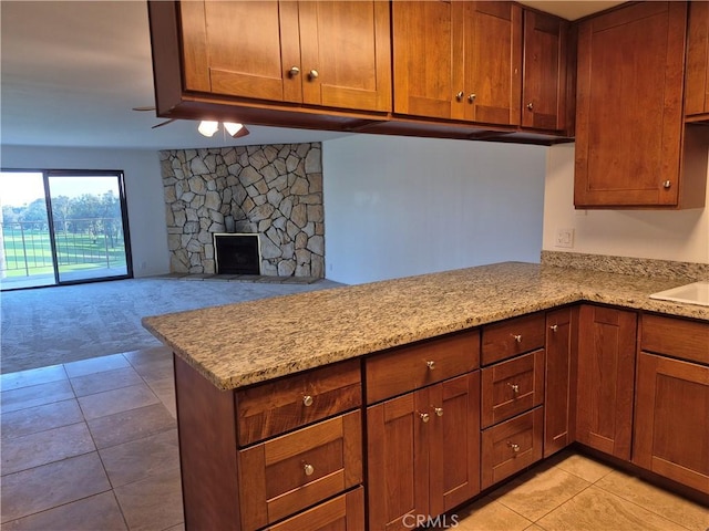 kitchen with kitchen peninsula, light stone counters, a stone fireplace, and light colored carpet