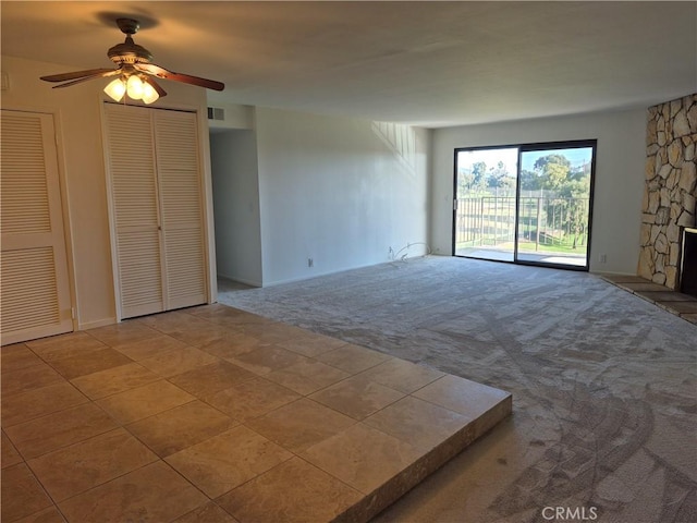 spare room featuring light carpet, a stone fireplace, and ceiling fan