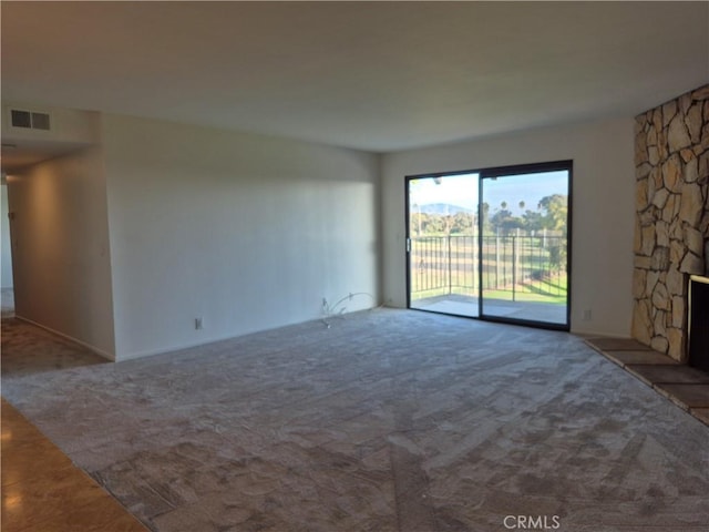 carpeted empty room with a stone fireplace