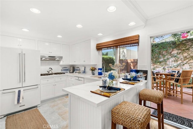 kitchen with a breakfast bar, white appliances, sink, kitchen peninsula, and white cabinetry