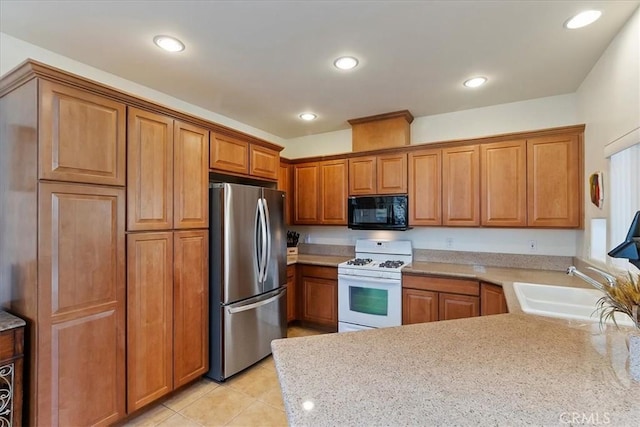 kitchen with stainless steel fridge, light stone counters, white range with gas cooktop, sink, and light tile patterned floors