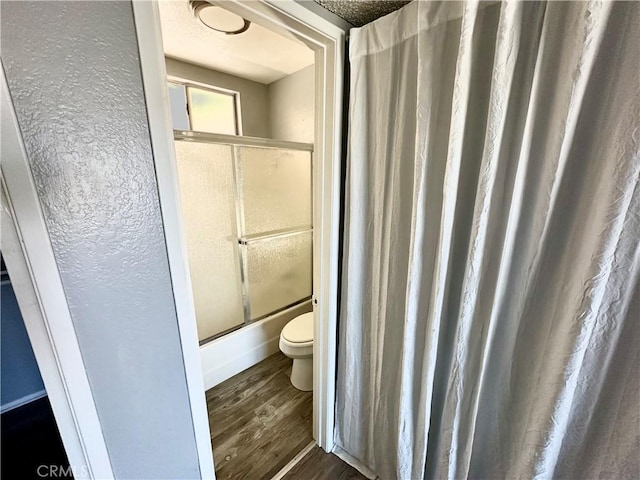 bathroom with hardwood / wood-style floors, enclosed tub / shower combo, and toilet