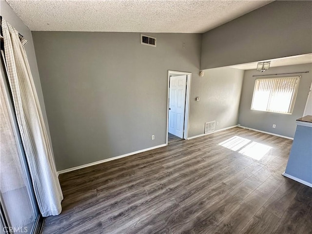 spare room with a textured ceiling, dark wood-type flooring, and vaulted ceiling