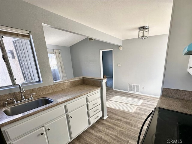 kitchen featuring a textured ceiling, sink, wood-type flooring, range, and white cabinetry