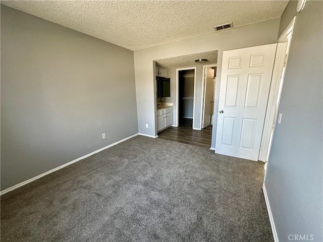 unfurnished bedroom with dark colored carpet, a textured ceiling, and ensuite bath