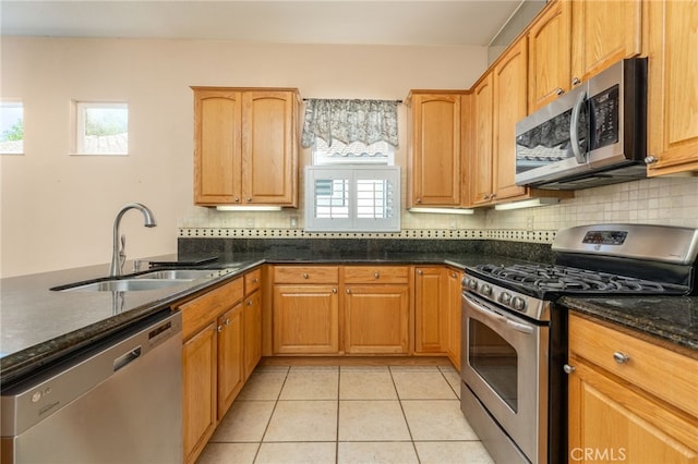 kitchen featuring decorative backsplash, dark stone counters, stainless steel appliances, sink, and light tile patterned floors