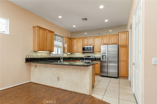 kitchen with kitchen peninsula, tasteful backsplash, dark stone counters, stainless steel appliances, and light tile patterned floors