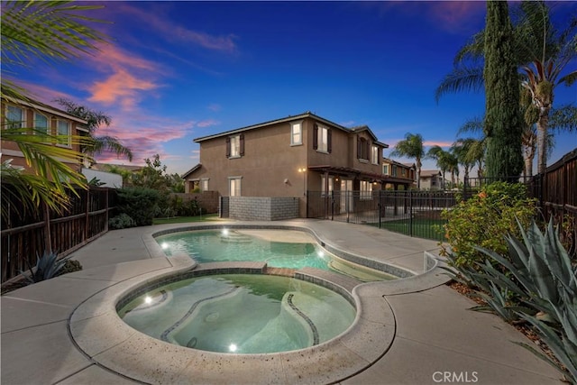 pool at dusk featuring an in ground hot tub and a patio area