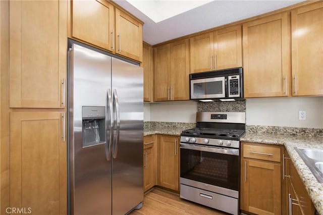 kitchen featuring stainless steel appliances, light stone counters, light hardwood / wood-style floors, and sink