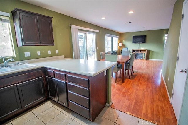 kitchen featuring kitchen peninsula, sink, light tile patterned floors, and dark brown cabinets