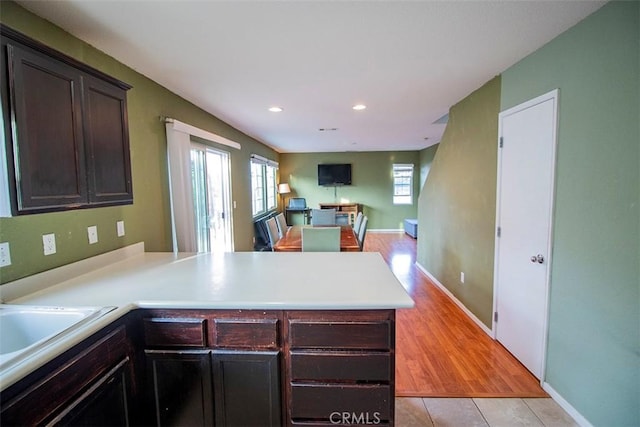 kitchen featuring kitchen peninsula, dark brown cabinetry, light tile patterned flooring, and sink