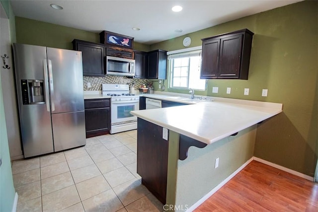 kitchen with sink, a breakfast bar area, decorative backsplash, kitchen peninsula, and stainless steel appliances