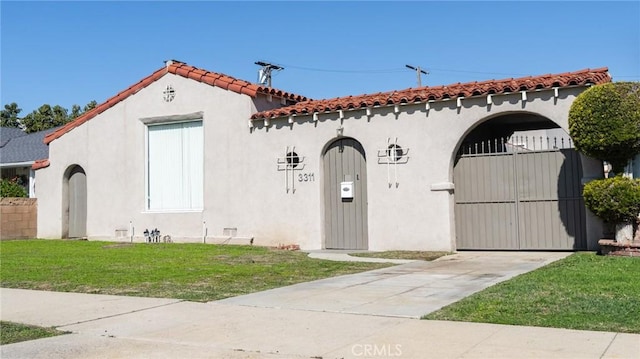 mediterranean / spanish-style house with fence, a tiled roof, a gate, stucco siding, and a front lawn