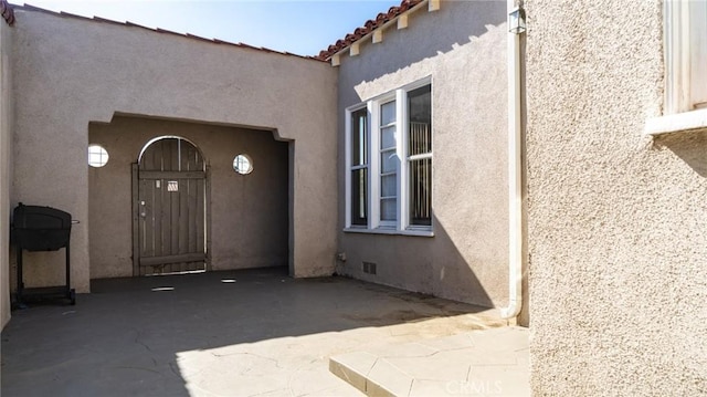 view of exterior entry with a tile roof, visible vents, and stucco siding