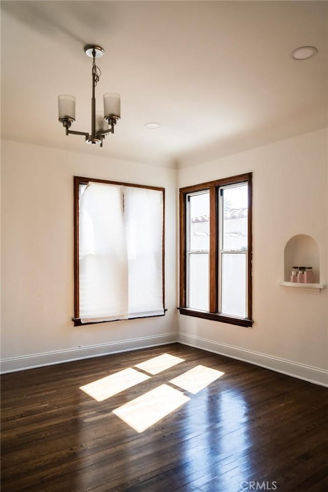 spare room with dark wood-type flooring, baseboards, and an inviting chandelier