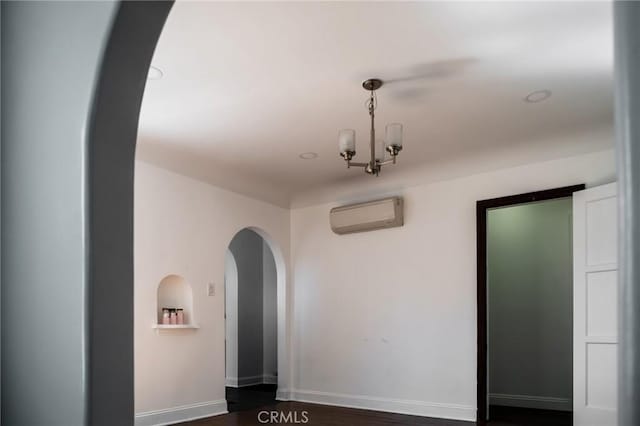 spare room featuring an inviting chandelier, baseboards, arched walkways, and a wall mounted AC