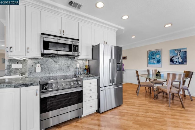 kitchen featuring stainless steel appliances, white cabinetry, and dark stone counters