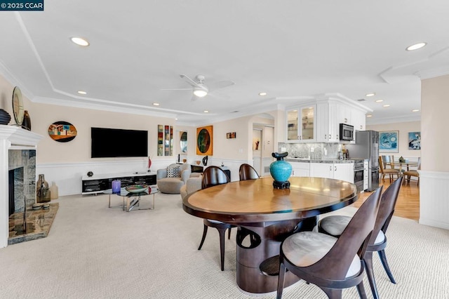 dining space featuring ceiling fan, ornamental molding, light carpet, and a high end fireplace