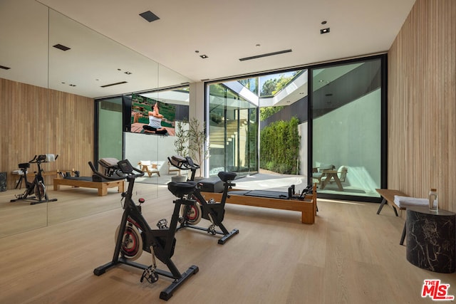 workout area featuring light hardwood / wood-style floors, expansive windows, and wooden walls