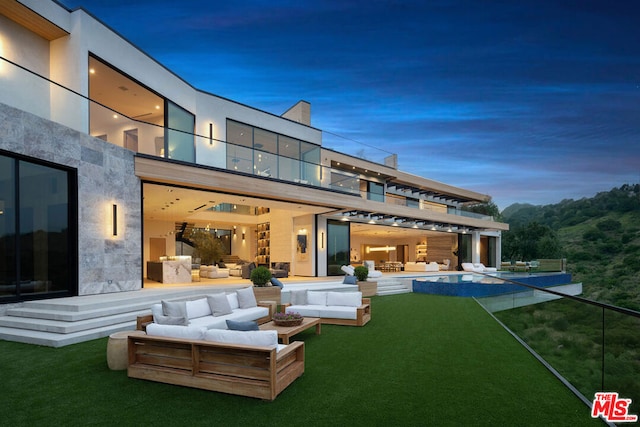 back house at dusk featuring a yard, an outdoor living space, and a balcony