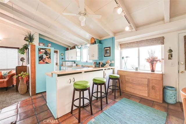 kitchen featuring a kitchen bar, kitchen peninsula, white cabinetry, and vaulted ceiling with beams