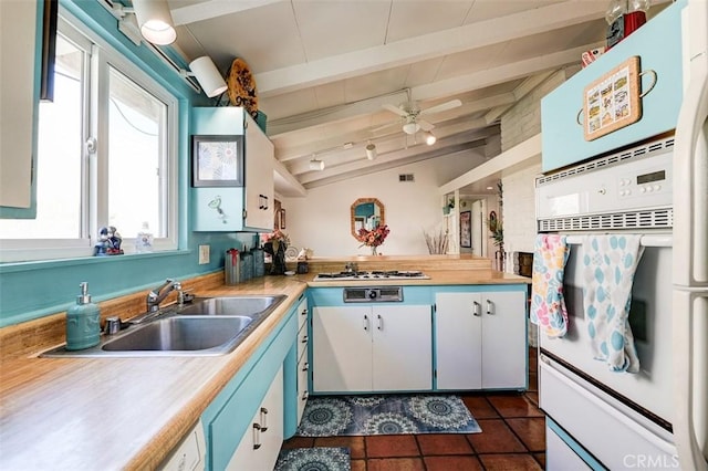 kitchen featuring ceiling fan, sink, lofted ceiling with beams, white cabinetry, and oven