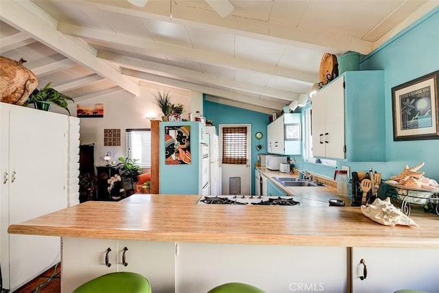 kitchen with sink, stainless steel gas cooktop, lofted ceiling with beams, kitchen peninsula, and white cabinets