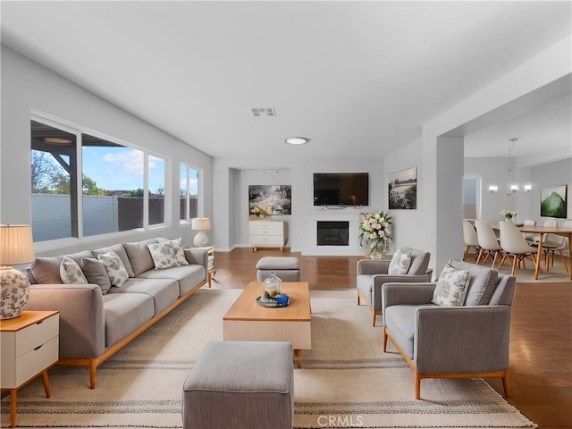 living area with light wood-style flooring, visible vents, a glass covered fireplace, and a notable chandelier