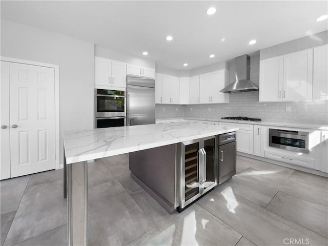 kitchen with wine cooler, white cabinetry, wall chimney exhaust hood, appliances with stainless steel finishes, and decorative backsplash