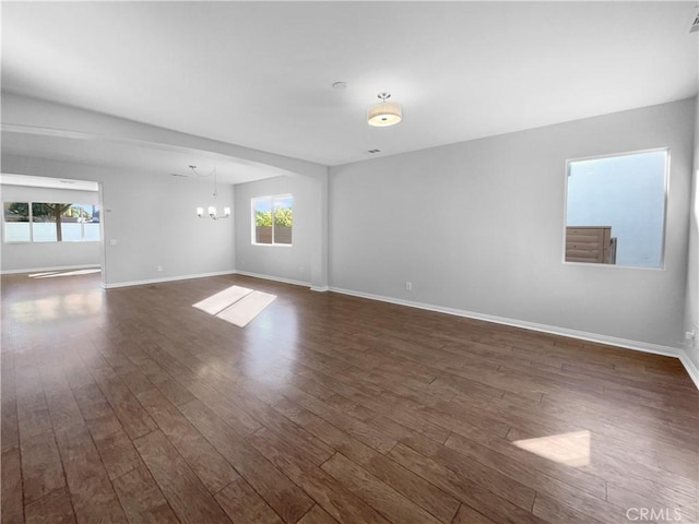 empty room with dark wood-type flooring, baseboards, a chandelier, and visible vents