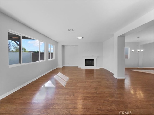 unfurnished living room with baseboards, visible vents, wood finished floors, and an inviting chandelier