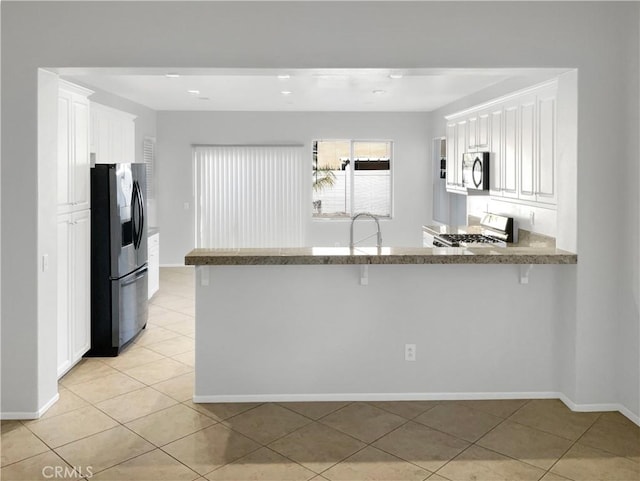 kitchen featuring a breakfast bar area, light tile patterned flooring, stainless steel appliances, a peninsula, and white cabinets