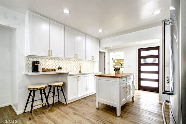 kitchen featuring wooden counters, light hardwood / wood-style flooring, stainless steel fridge, white cabinetry, and a breakfast bar area