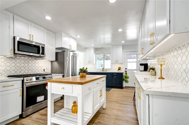 kitchen featuring high end appliances, sink, a center island, white cabinetry, and butcher block counters