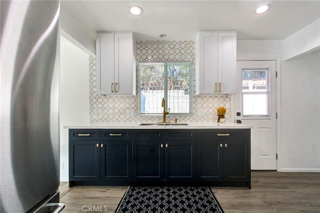 kitchen with decorative backsplash, white cabinetry, stainless steel refrigerator, and sink