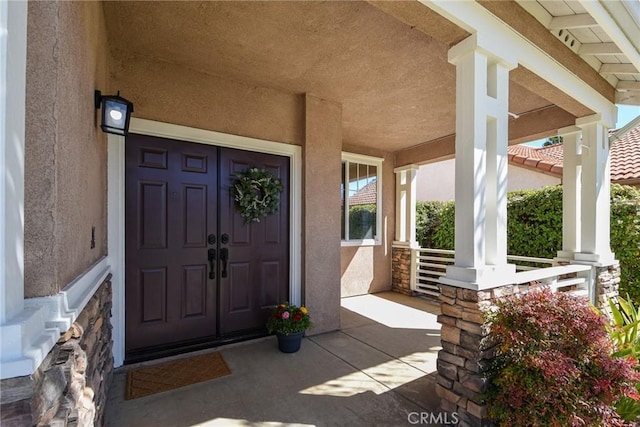 doorway to property featuring covered porch and stucco siding