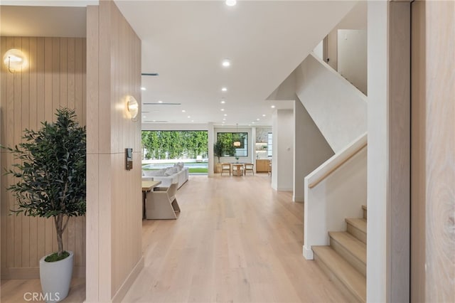 corridor with light hardwood / wood-style flooring, a wall of windows, and wooden walls