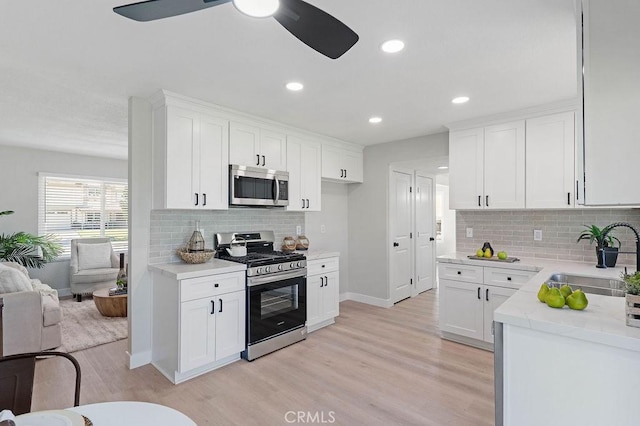 kitchen featuring appliances with stainless steel finishes, light wood-type flooring, tasteful backsplash, sink, and white cabinetry