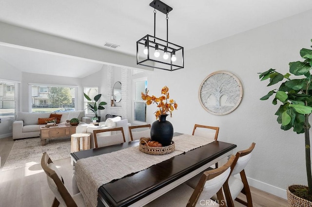 dining area featuring a fireplace, light hardwood / wood-style floors, and vaulted ceiling