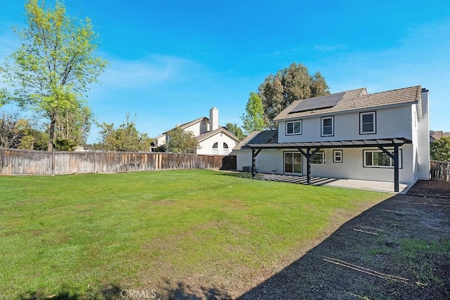 back of house featuring solar panels, a patio area, and a lawn