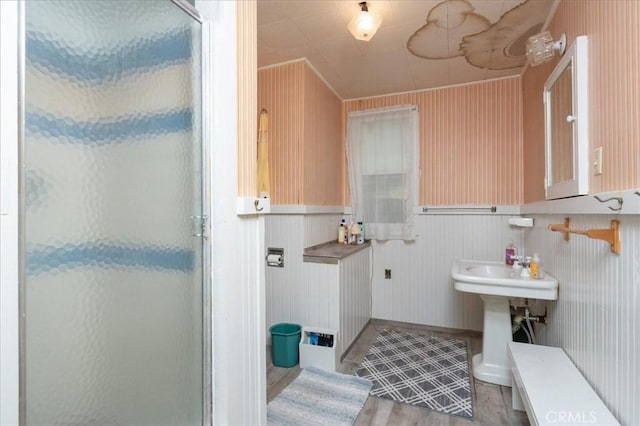 bathroom with hardwood / wood-style floors, a shower with shower door, ornamental molding, and wooden walls