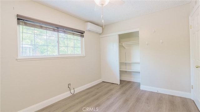 unfurnished bedroom with a wall mounted air conditioner, ceiling fan, light hardwood / wood-style flooring, and a closet