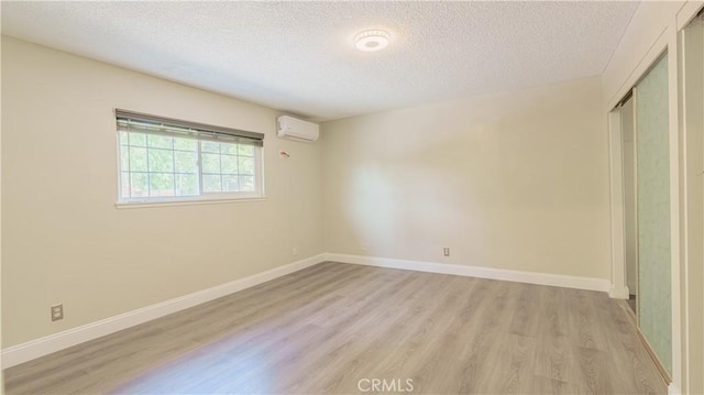 unfurnished bedroom with a textured ceiling, light hardwood / wood-style flooring, an AC wall unit, and a closet