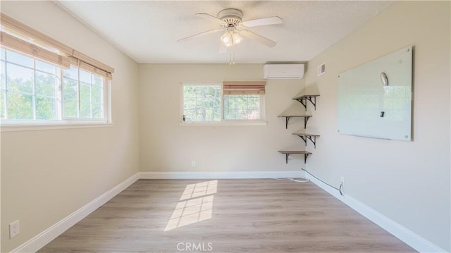 spare room with an AC wall unit, ceiling fan, and light hardwood / wood-style floors