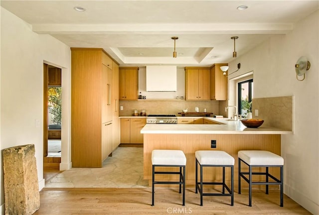 kitchen featuring hanging light fixtures, range hood, kitchen peninsula, light brown cabinetry, and light wood-type flooring