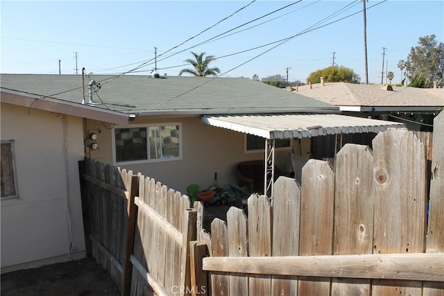 view of side of home featuring stucco siding, a shingled roof, and fence