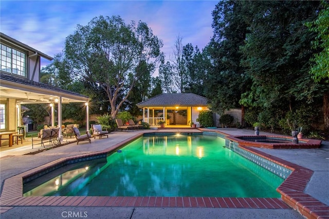 pool at dusk with a patio area, an outdoor structure, and an in ground hot tub