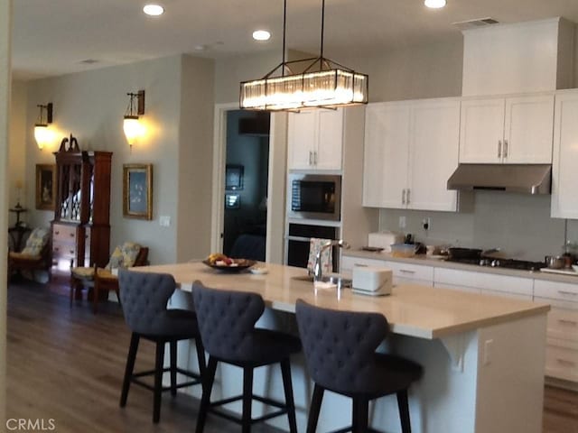 kitchen featuring a kitchen island with sink, built in microwave, wall oven, white cabinetry, and gas cooktop