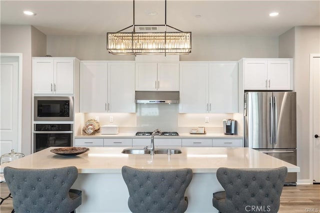 kitchen featuring appliances with stainless steel finishes, white cabinetry, hanging light fixtures, and an island with sink