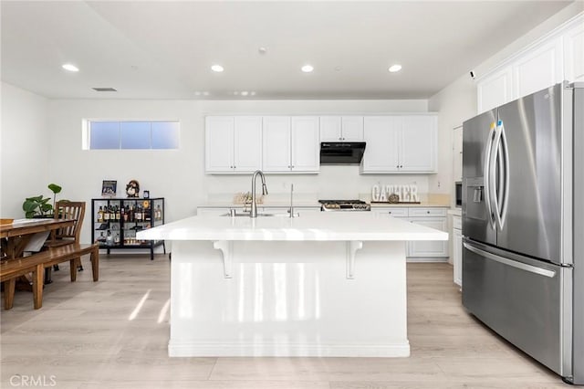 kitchen with sink, a kitchen breakfast bar, stainless steel fridge, an island with sink, and white cabinets